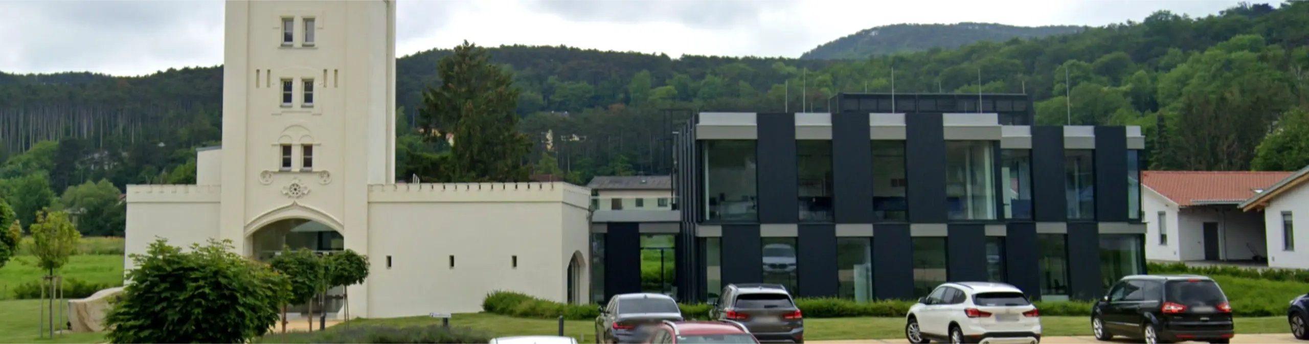 Modernes Bürogebäude mit Glasfassade neben historischem weißem Turm – Firmensitz von Krüger Austria