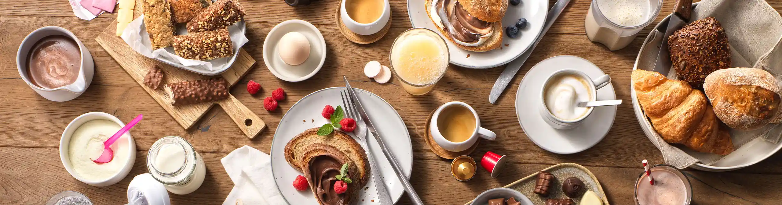 Draufsicht auf reichhaltiges Frühstückstisch mit Kaffee, Croissants, Schokolade, Snacks und Fruchtsäften